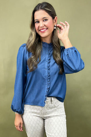 Woman wearing a blue blouse and light gray pants against a beige background