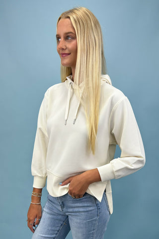 Woman wearing a white hoodie and blue jeans against a light blue background