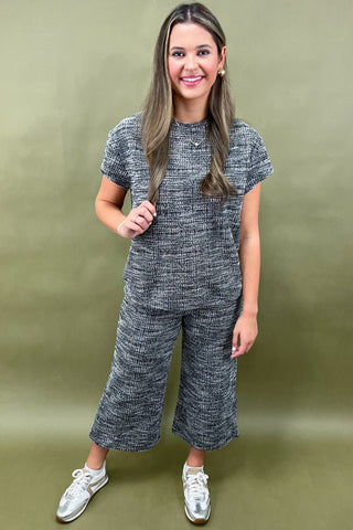 Woman wearing a gray knit outfit with wide-leg pants against an olive green background