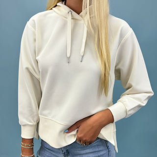 Person wearing a white hoodie and blue jeans against a gray background
