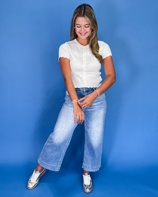 Woman wearing a white top and blue jeans against a blue background