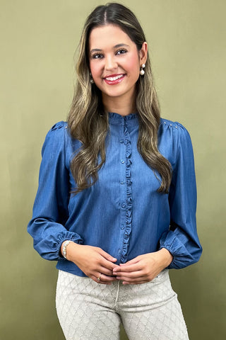 Woman wearing a blue blouse and white pants against a beige background