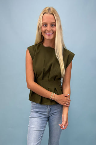 Woman wearing an olive green sleeveless top and light blue jeans against a plain background