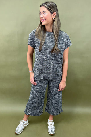 Woman wearing a gray knit outfit with white sneakers on a green background