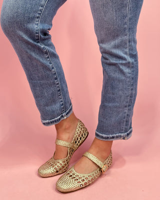 Gold flats worn with blue jeans on a pink background