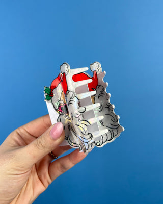 Shop the Santa Hair Clip featuring a pearlescent Santa design, pink heart sunglasses, and festive holiday details. A cute Christmas claw clip!