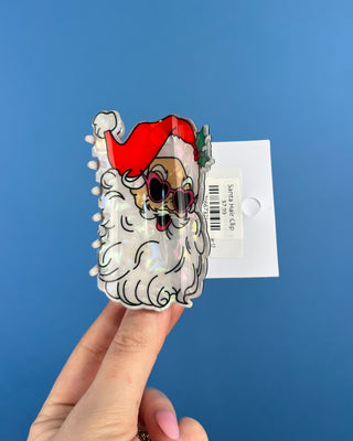 Shop the Santa Hair Clip featuring a pearlescent Santa design, pink heart sunglasses, and festive holiday details. A cute Christmas claw clip!