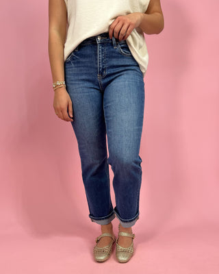 Person wearing blue jeans and a white top on a pink background