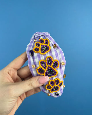 Shop the Purple Gingham Gameday Headband featuring sparkling purple and gold beaded paw prints, rhinestones, and a trendy knotted design. Perfect for game day!