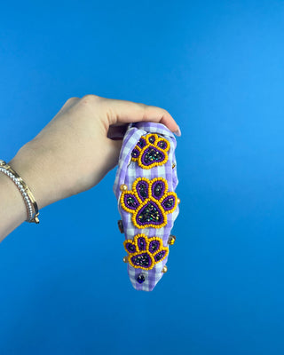Shop the Purple Gingham Gameday Headband featuring sparkling purple and gold beaded paw prints, rhinestones, and a trendy knotted design. Perfect for game day!