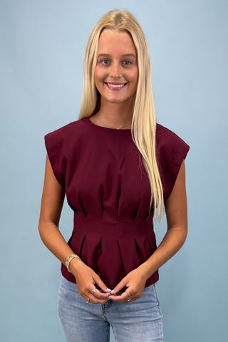 Woman wearing a burgundy peplum top against a light blue background