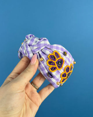 Shop the Purple Gingham Gameday Headband featuring sparkling purple and gold beaded paw prints, rhinestones, and a trendy knotted design. Perfect for game day!
