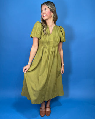 Olive green maxi dress with a V-neckline, pintuck detailing, short puff sleeves, and a flowy silhouette.