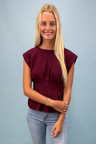 Woman wearing a burgundy top and light blue jeans against a gray background