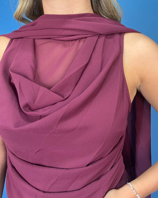 A close-up of a woman wearing a sleeveless draped top in a dusty plum purple color, showing the back drape and sheer mesh detail
