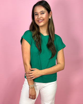 Woman wearing a green shirt and white pants against a pink background