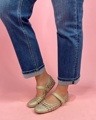 Gold flats worn with blue jeans on a pink background
