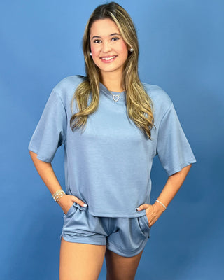 A woman modeling a matching light blue lounge set consisting of a short-sleeve crewneck top and matching short