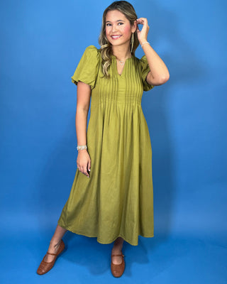 Olive green maxi dress with a V-neckline, pintuck detailing, short puff sleeves, and a flowy silhouette.
