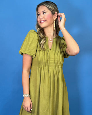 Olive green maxi dress with a V-neckline, pintuck detailing, short puff sleeves, and a flowy silhouette.