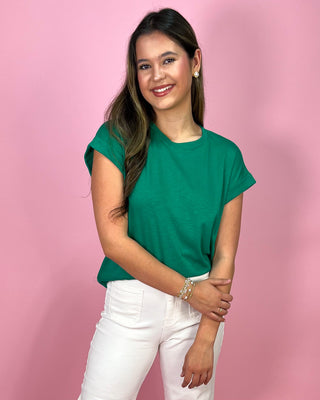 Woman wearing a green top and white pants against a pink background