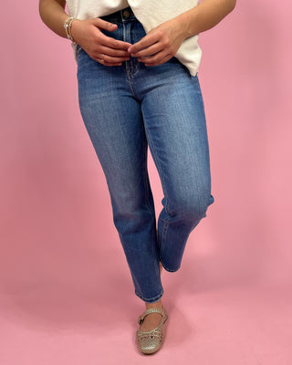 Person wearing blue jeans and a white shirt on a pink background