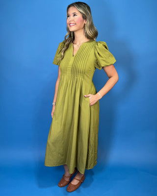 Olive green maxi dress with a V-neckline, pintuck detailing, short puff sleeves, and a flowy silhouette.