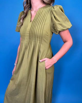 Olive green maxi dress with a V-neckline, pintuck detailing, short puff sleeves, and a flowy silhouette.