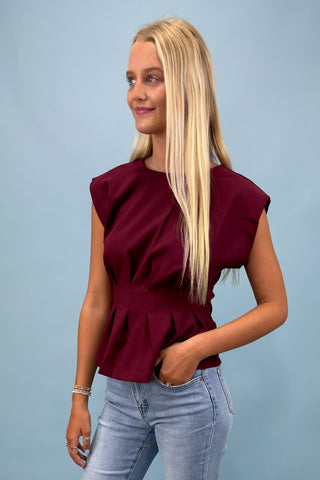 Woman wearing a burgundy top and light blue jeans against a plain background