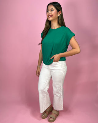 Woman wearing a green top and white pants against a pink background