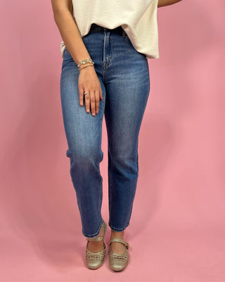 Person wearing blue jeans and a white top on a pink background