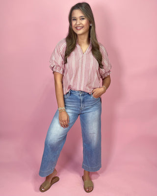Woman wearing a striped shirt and jeans against a pink background
