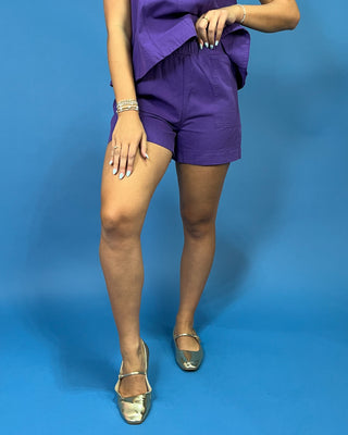 A person wearing a purple short-sleeve top and matching purple shorts