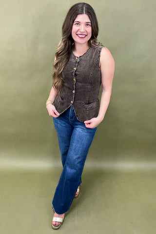 Woman wearing a brown vest and blue jeans against a green background