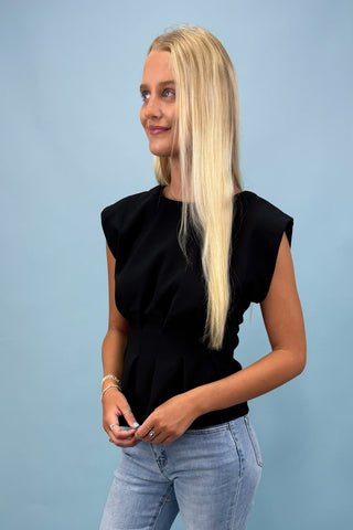 Woman wearing a black sleeveless top and light blue jeans against a light blue background