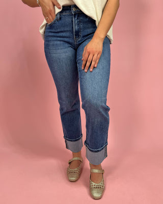 Person wearing blue jeans and gold sandals on a pink background