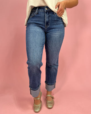 Person wearing blue jeans and gold shoes on a pink background