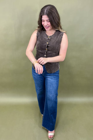Woman wearing a brown vest and blue jeans against a green background