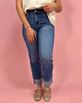 Person wearing blue jeans and a white top on a pink background