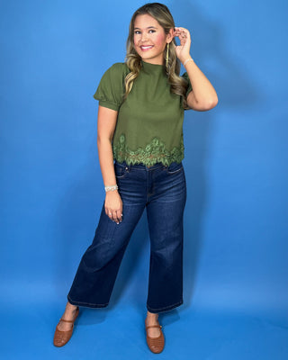 Olive green puff sleeve knit top with mock neckline and delicate lace hem detail, styled with dark wash jeans.