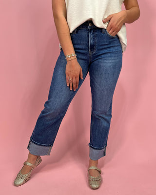 Person wearing blue jeans and a white top on a pink background