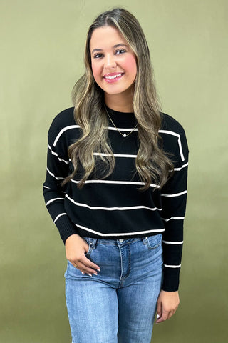 Woman wearing a black and white striped sweater and blue jeans against a green background