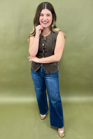 Woman wearing a sleeveless brown top and blue jeans against a green background