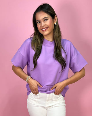 Woman wearing a purple shirt and white pants against a pink background