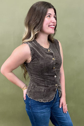 Woman wearing a brown sleeveless vest over a blue top against a green background