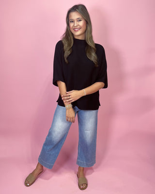 Woman wearing a black top and blue jeans against a pink background