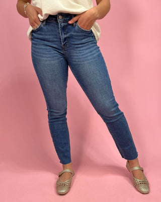 Person wearing blue jeans and a white top on a pink background