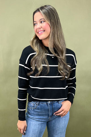 Woman wearing a black and white striped sweater and blue jeans against a green background