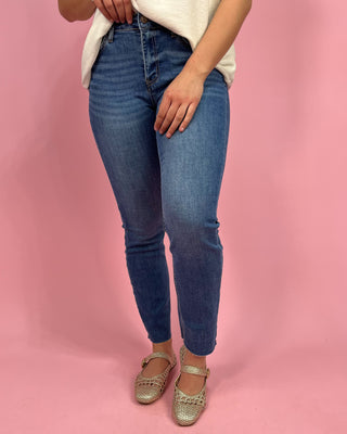 Person wearing blue jeans and gold sandals on a pink background