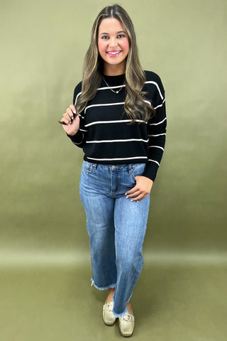 Woman wearing a black and white striped sweater and blue jeans against a green background